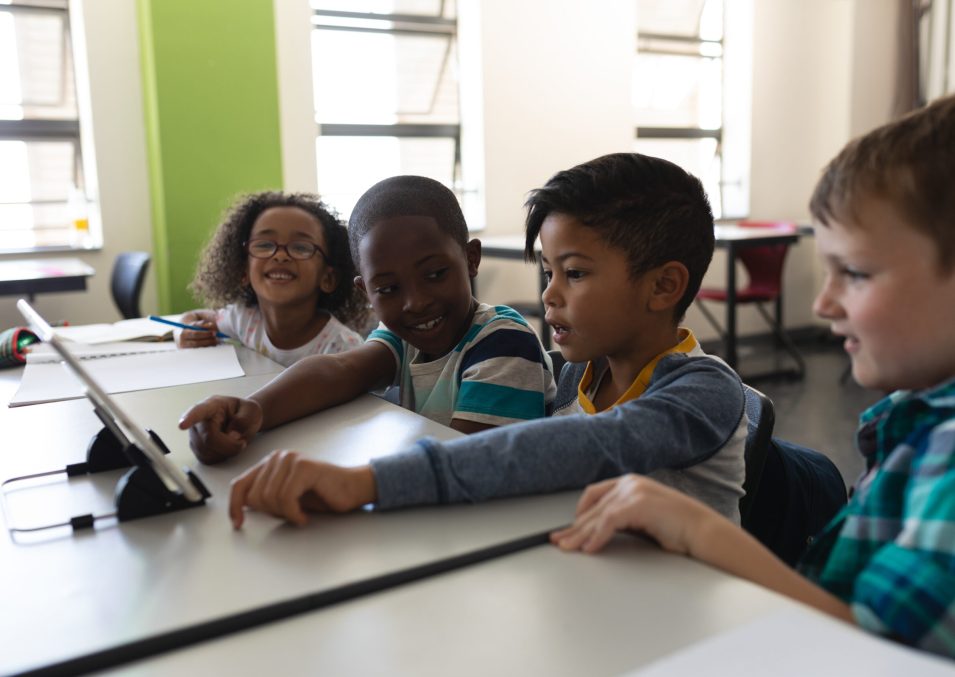 Side view of curious schoolkids studying on digital tablet while sitting at desk in classroom of elementary school